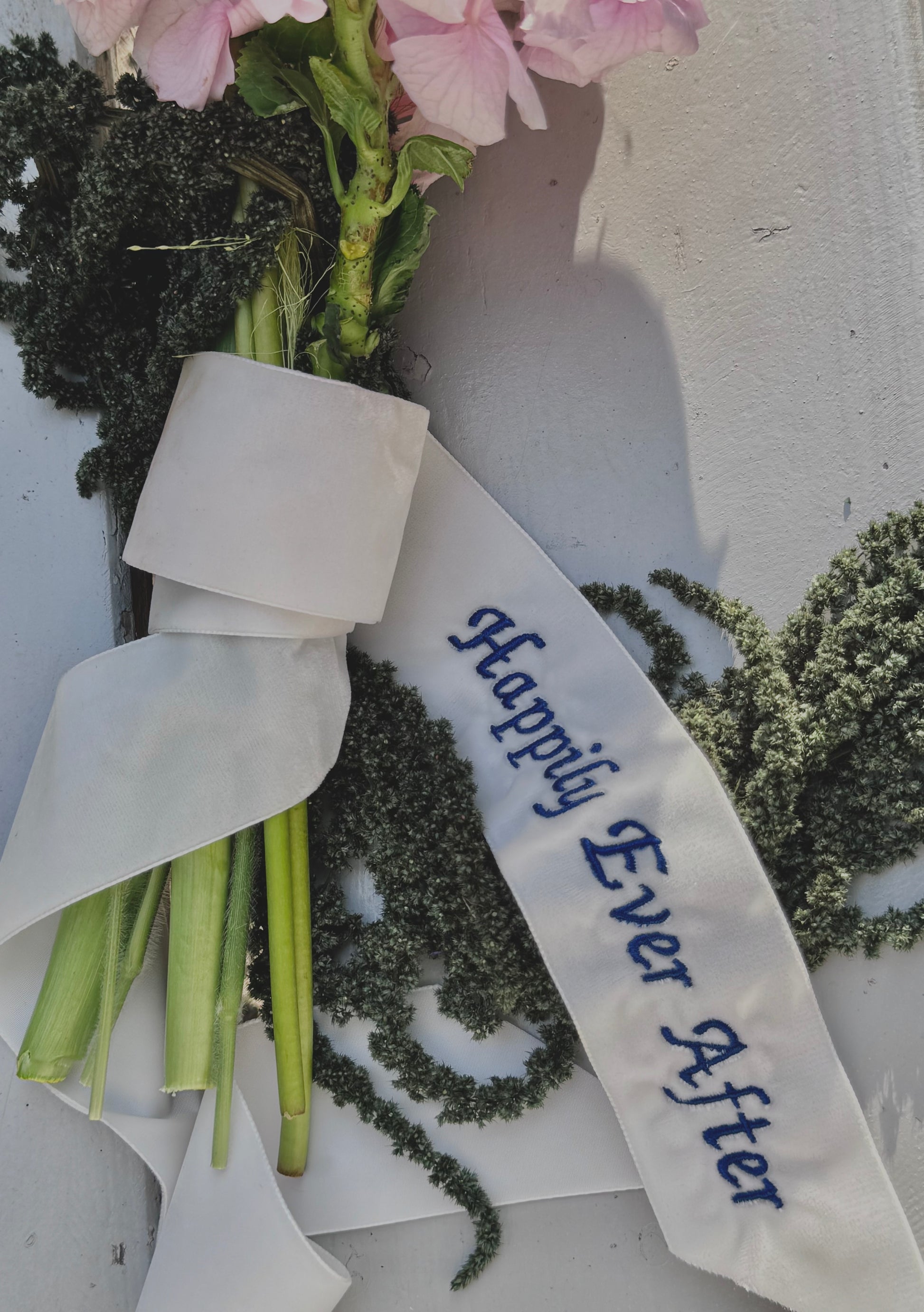 Zbliżenie na bukiet owinięty aksamitną wstążką z napisem „Happily Ever After”