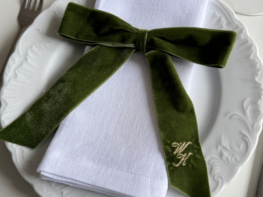 Zielona aksamitna kokarda z haftowanymi inicjałami na białej serwetce
